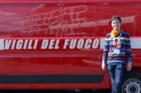 Volontario FAI con una maglia a righe e jeans scuri davanti al camion dei vigili del fuoco rosso