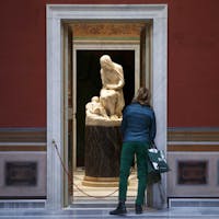 Visitatrice alle Giornate FAI al Teatro Torlonia | Foto Musacchio © FAI Una visitatrice al Teatro Torlonia di Roma che indossa una camicia blu e pantaloni verde. La stanza ha le pareti bordeaux con una porta di marmo aperta che lascia intravedere una scultura