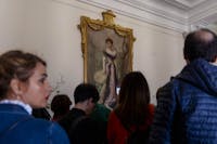 Primo piano di visitatori tra cui una donna con capelli biondi, rossetto rosso e giacca azzurro. Sullo sfondo si scorge una grande dipinto antico con una donna con abito lungo di altri tempi